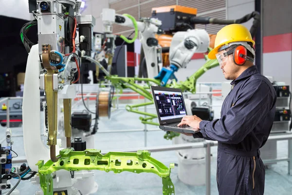 Engineer using laptop computer maintenance automatic robotic hand machine tool in automotive industry, Smart factory concept