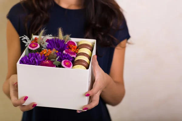 Mujer sosteniendo una caja con flores y galletas de macarrones — Foto de Stock