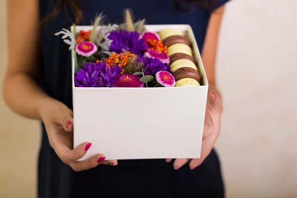 Mulher segurando uma caixa com flores e biscoitos macaroon — Fotografia de Stock