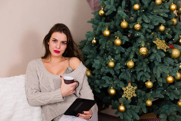 Woman reading e-book near the Christmas tree — Stock Photo, Image