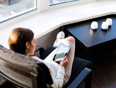 Bir e-kitap ile cam kenarında oturan kadın