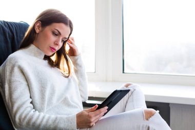 Bir e-kitap ile cam kenarında oturan kadın