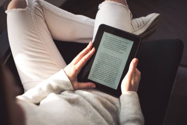 Bir e-kitap ile cam kenarında oturan kadın