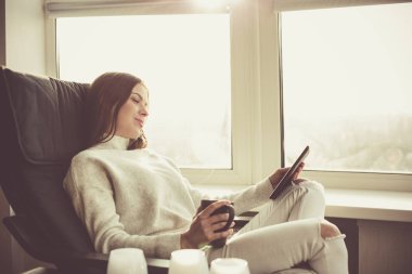 Bir e-kitap ile cam kenarında oturan kadın
