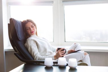 Bir e-kitap ile cam kenarında oturan kadın