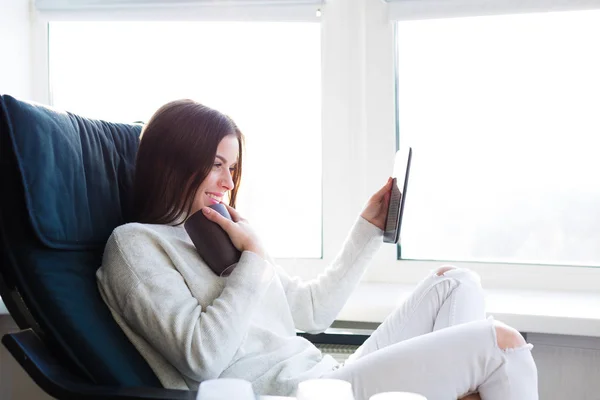 Woman sitting by the window with an e-book — Stock Photo, Image