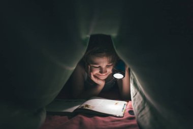 Gülümse küçük kız battaniyenin altında bir kitap okunuyor.