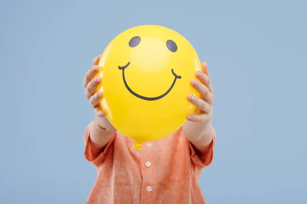 Niño pequeño cubriendo la cara con globo amarillo con sonrisa — Foto de Stock