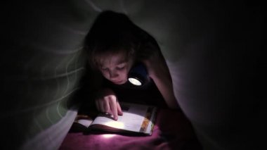 Küçük kız elinde fenerle kitap okuyor.