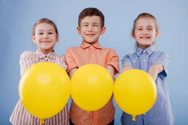 Trzy szczęśliwe dzieci dziewczyny i chłopiec z żółtymi balonami — Zdjęcie stockowe