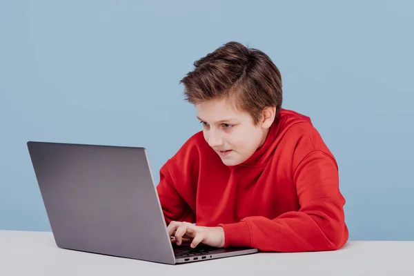 Концентрированный мальчик в красной толстовке печатает на ноутбуке — стоковое фото