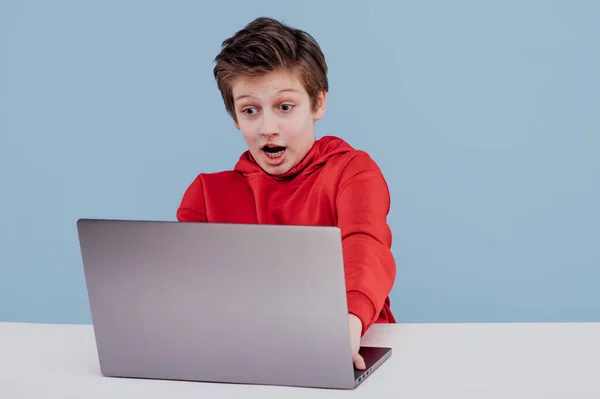 Возбужденный мальчик с ноутбуком в студии синий фон — стоковое фото