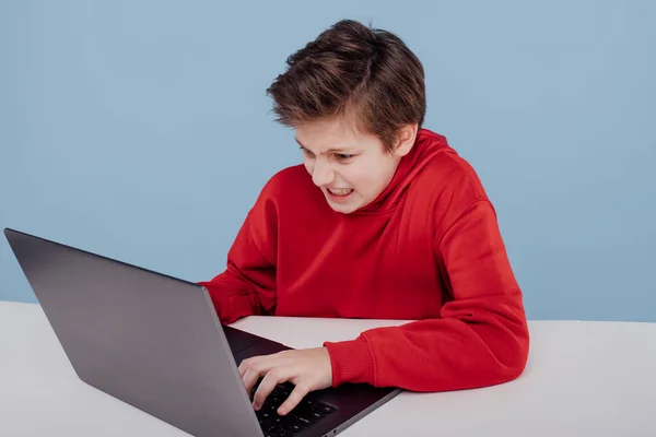 Раздражённый мальчик в красной толстовке печатает на ноутбуке — стоковое фото