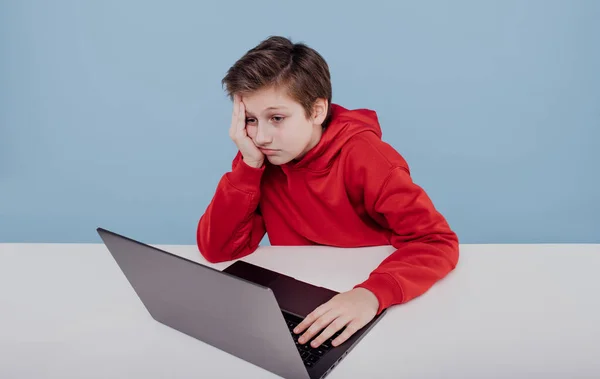 Dizüstü bilgisayarın yanındaki kırmızı tişörtlü yorgun çocuk. — Stok fotoğraf