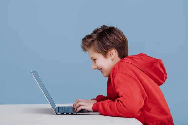 Kırmızı tişörtlü mutlu çocuk dizüstü bilgisayarda oynuyor., — Stok fotoğraf