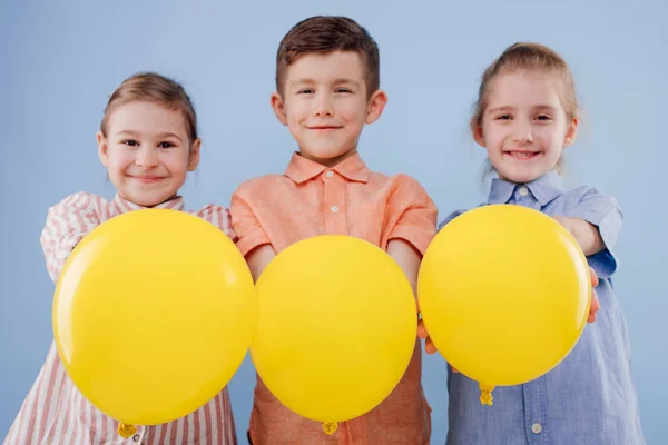 Trzy szczęśliwe dzieci dziewczyna i chłopiec z żółtym balonem z uśmiechem. — Zdjęcie stockowe