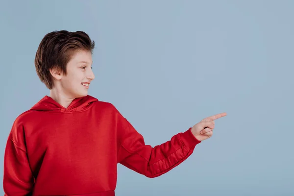 Happy teen boy in red sweatshirt pointing with finger in side — Stock Photo, Image