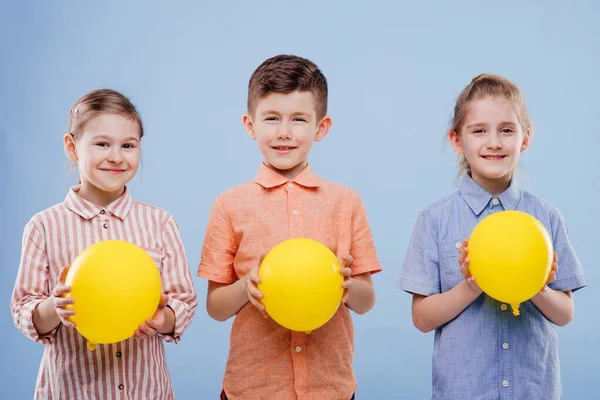 Três crianças com balões amarelos com um sorriso . — Fotografia de Stock
