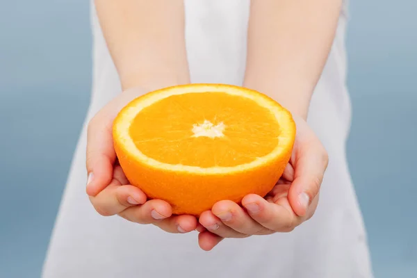 Cerca, media naranja en las manos de las niñas aisladas en azul —  Fotos de Stock