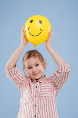 little girl holds up yellow balloon with smile.