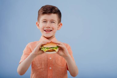 little boy smiles with sandwich in hand.