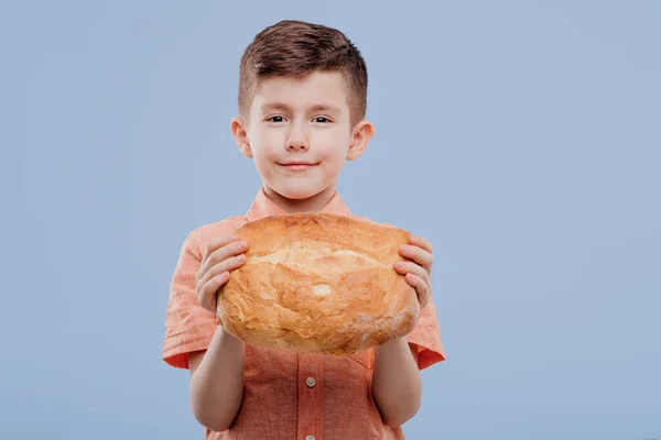 Child little boy holding a bread,on blue background, copy space — 图库照片