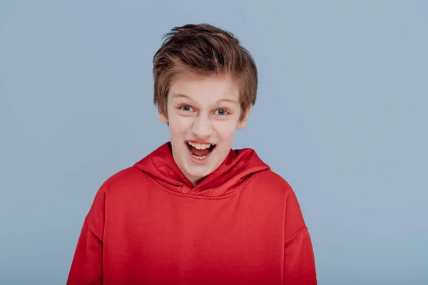 Boy screaming in red sweatshirt, isolated on blue background — Stockfoto