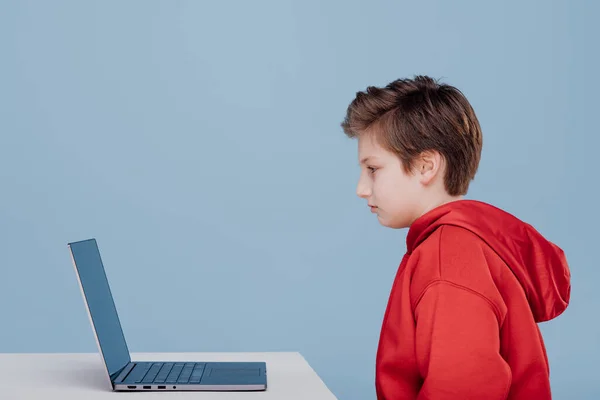 Boy n red sweatshirt looks at laptop — Zdjęcie stockowe