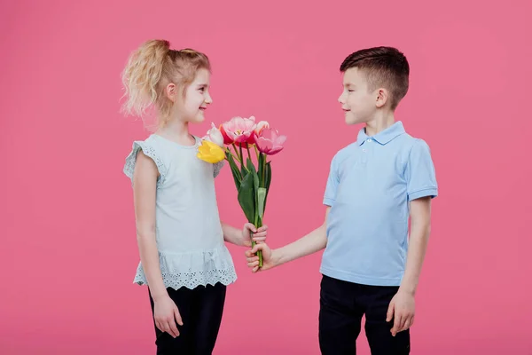 Boy giving flowers to girl pink background — Stock Photo, Image