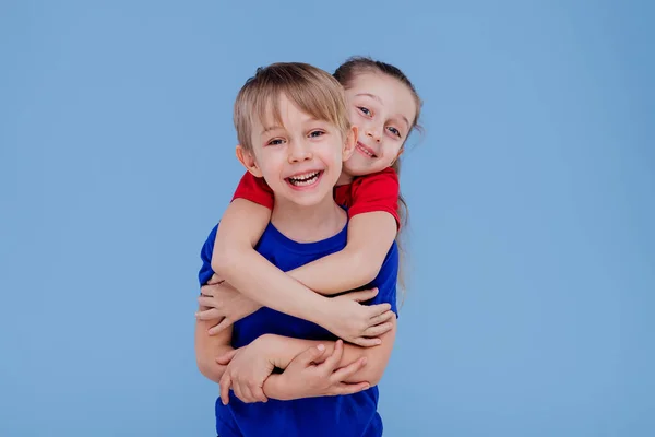 Happy little girl siblings hugging little boy isolated on blue background,