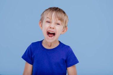 Küçük çocuk çığlık atarak kameraya baktı. Mavi tişört giymişti.
