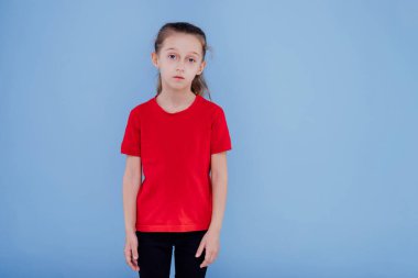 Kırmızı tişört giymiş üzgün küçük kız, mavi arka planda izole edilmiş.,