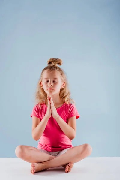 Kleines Mädchen meditiert in Yoga-Pose, isoliert auf blauem Grund — Stockfoto