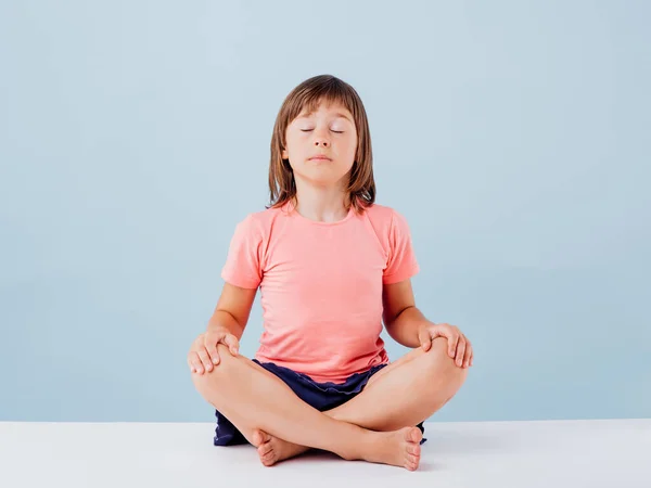 Kleines Mädchen praktiziert Yoga, isoliert auf blauem Hintergrund, — Stockfoto