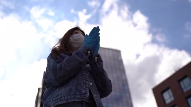 Applaus. meisje met handschoenen en medisch masker applaus over de stad achtergrond. — Stockvideo