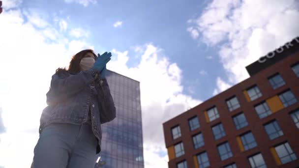 Aplausos. Mujer con guantes y máscara médica aplausos sobre fondo de la ciudad . — Vídeo de stock