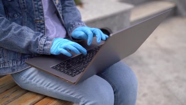 Close up, κορίτσι με γάντια και ιατρική μάσκα χρησιμοποιεί φορητό υπολογιστή έξω — Αρχείο Βίντεο