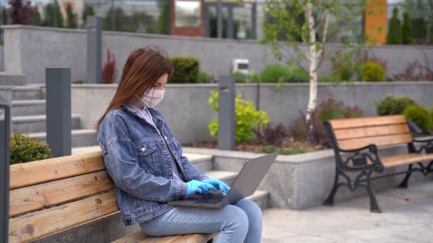 Chica en guantes y máscara médica utiliza el ordenador portátil fuera — Vídeos de Stock