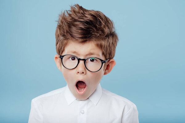 Surprised little boy in eyeglasses on blue background