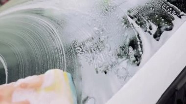 Adamın eli sünger ve köpükle arabanın ön camını siler. Otomobil servisi kavramı,
