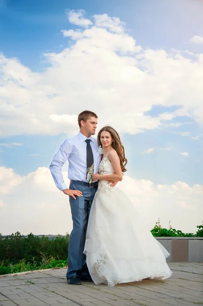 Düğün günü. Güzel gelin damat gökyüzü arka plan üzerinde kollarında — Stok fotoğraf