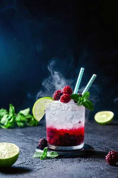 Cocktail au rhum ou vodka, soda, purée de framboises et mûres, chaux et menthe dans le verre avec fumée sur fond gris foncé — Photo