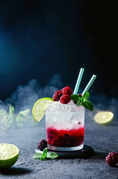 Cocktail au rhum ou vodka, soda, purée de framboises et mûres, chaux et menthe dans le verre avec fumée sur fond gris foncé — Photo