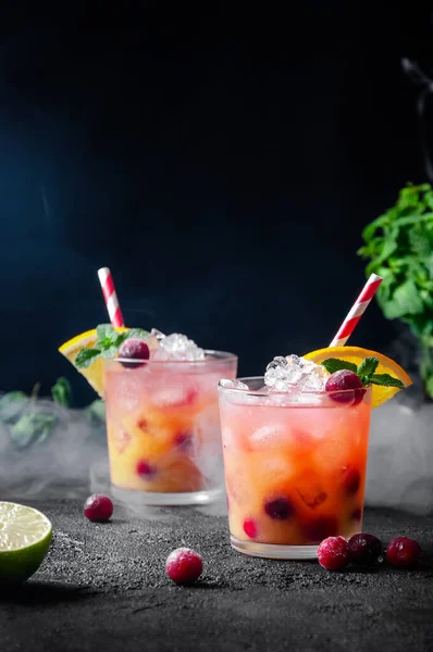 Cocktail avec rhum ou vodka, soda, canneberge, jus d'orange, chaux et menthe dans le verre avec fumée sur fond gris foncé — Photo