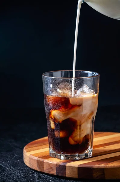 Melk wordt gegoten in ijskoffie in groot glas op donkere achtergrond. Concept Verfrissend zomerdrankje — Stockfoto