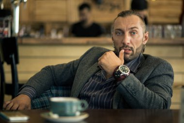 Sakallı, bir fincan kahve ile bir kafede oturan genç bir adam