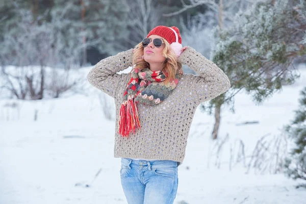 Mooi meisje in een rode hoed en trui in de sneeuw in roze met hoofdtelefoons en sjaal — Stockfoto