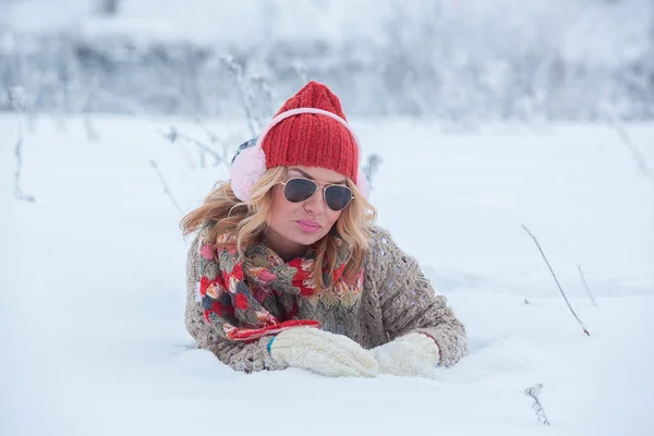 Mooi meisje in een rode hoed en trui in de sneeuw in roze met hoofdtelefoons en sjaal — Stockfoto
