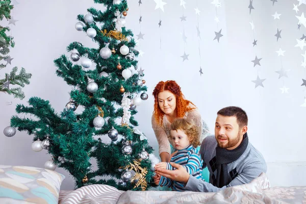 Navidad feliz familia de tres personas decorando abeto con cajas de regalo sobre fondo de dormitorio blanco — Foto de Stock