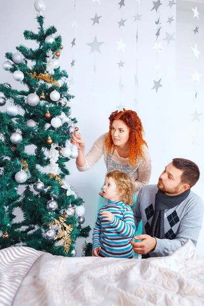 Navidad feliz familia de tres personas decorando abeto con cajas de regalo sobre fondo de dormitorio blanco — Foto de Stock